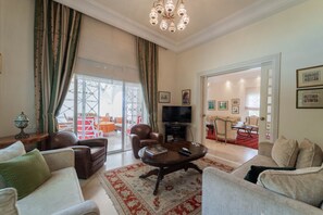 A spacious living room with a large television, comfortable seating, and a decorative chandelier. - Villa d'exception à Gammarth – piscine privée (Gammarth)