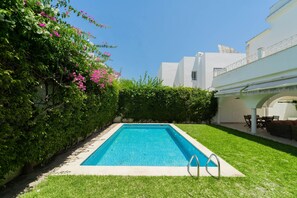 A rectangular swimming pool with a clear blue water surface, surrounded by well-maintained grass and a hedge with pink flowers. - Villa d'exception à Gammarth – piscine privée (Gammarth)