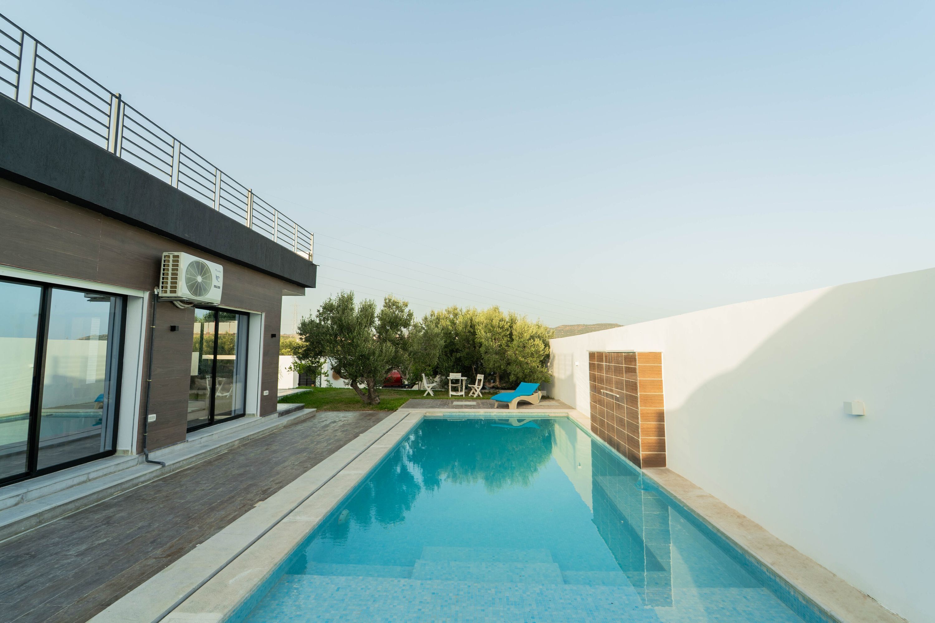 A modern building with a swimming pool, a covered patio, and a view of the surrounding landscape.