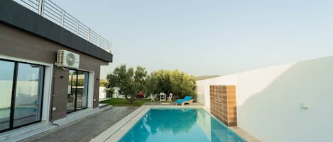 A modern building with a swimming pool, a covered patio, and a view of the surrounding landscape.