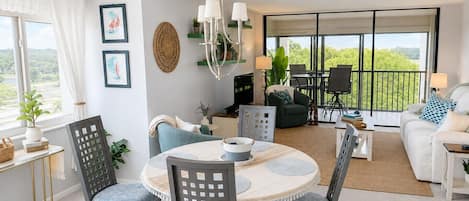A modern living room with a dining area, a sofa set, a fireplace, and a balcony with a view.