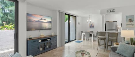 A modern living room with a flat-screen TV, a dining area, and a kitchen.