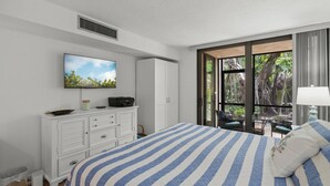 A bedroom with a bed, a television, a wardrobe, and a window with a view of greenery. - Sandy Cove Sanctuary | Renovated Ground-Floor Condo, Walk to Village, Private Beach & Fishing Pier (Siesta Key)