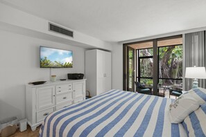 Ein Schlafzimmer mit einem Bett, einem Fernseher, einem Kleiderschrank und einem Fenster mit Blick ins Grüne.