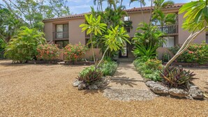A building with a tiled roof, surrounded by a gravel pathway, and various tropical plants. - Sandy Cove Sanctuary | Renovated Ground-Floor Condo, Walk to Village, Private Beach & Fishing Pier (Siesta Key)