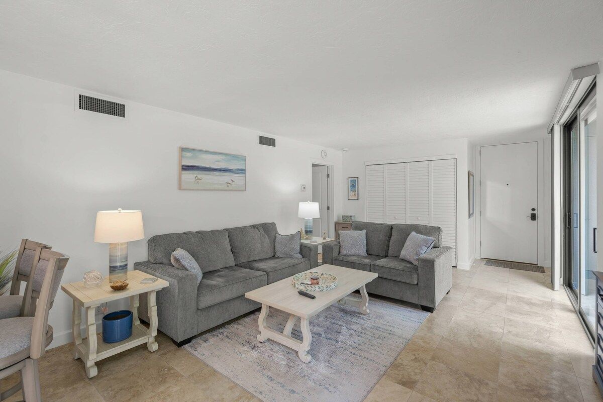 A living room with two grey sofas, a white coffee table, a side table with a lamp, and a painting on the wall.