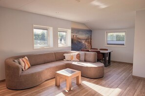 Ein modernes Wohnzimmer mit einer gebogenen Couch, einem kleinen Holztisch und einem Essbereich mit Tisch und Stühlen.
