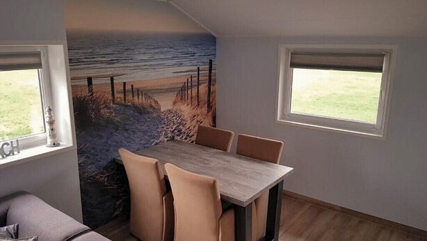 Un espace repas comprenant une table et des chaises, une fresque représentant une scène de plage et une fenêtre donnant sur l’extérieur.