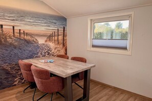 Ein Zimmer mit einem Meeresmotiv an der Wand, einem Holztisch mit Stühlen und einem Fenster mit Blick auf Bäume.