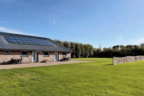 Ein modernes Gebäude mit flachem Dach, Solarpanels und einer gepflasterten Fläche mit Tisch und Stühlen.