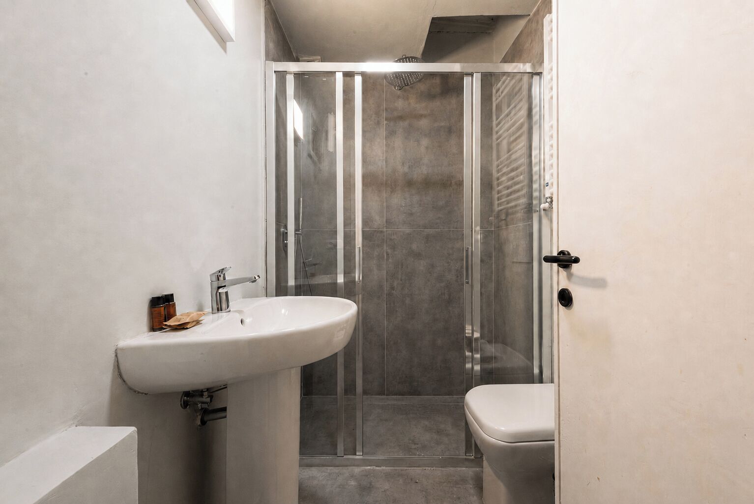 Um banheiro com pia branca, vaso sanitário e chuveiro com box de vidro.