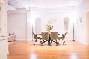 Uma ampla área de jantar com piso de madeira, uma mesa central com cadeiras e um vaso com flores.