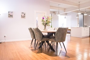 Ein moderner Essbereich mit einem Holztisch und vier Stühlen, einer Blumenvase und einer Küche im Hintergrund.