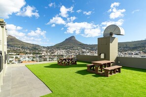 Eine Dachterrasse mit Kunstgras, Picknicktischen und einer Satellitenschüssel.