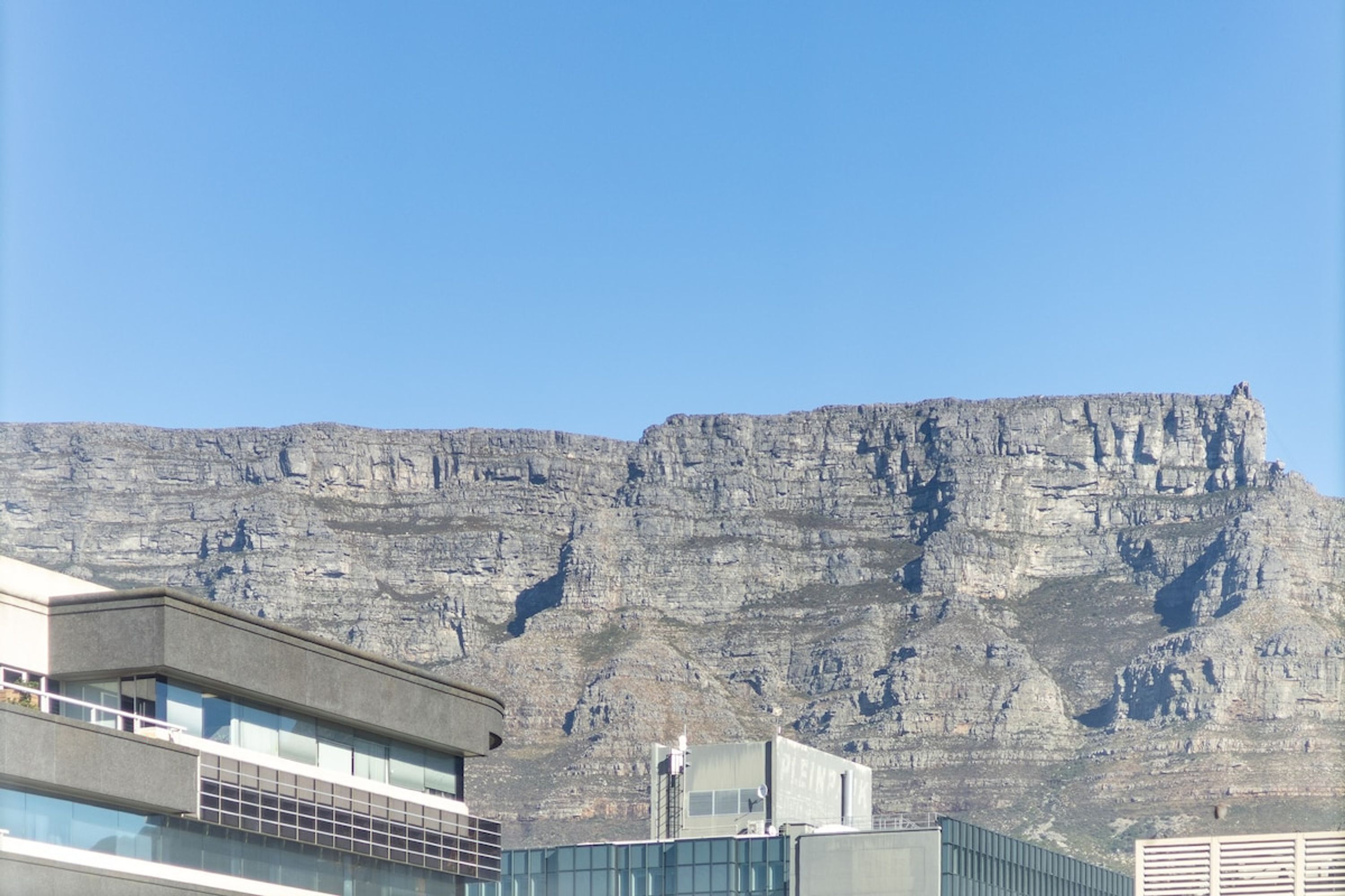 A modern building with a flat roof and large windows, situated in front of a large, rocky cliff.