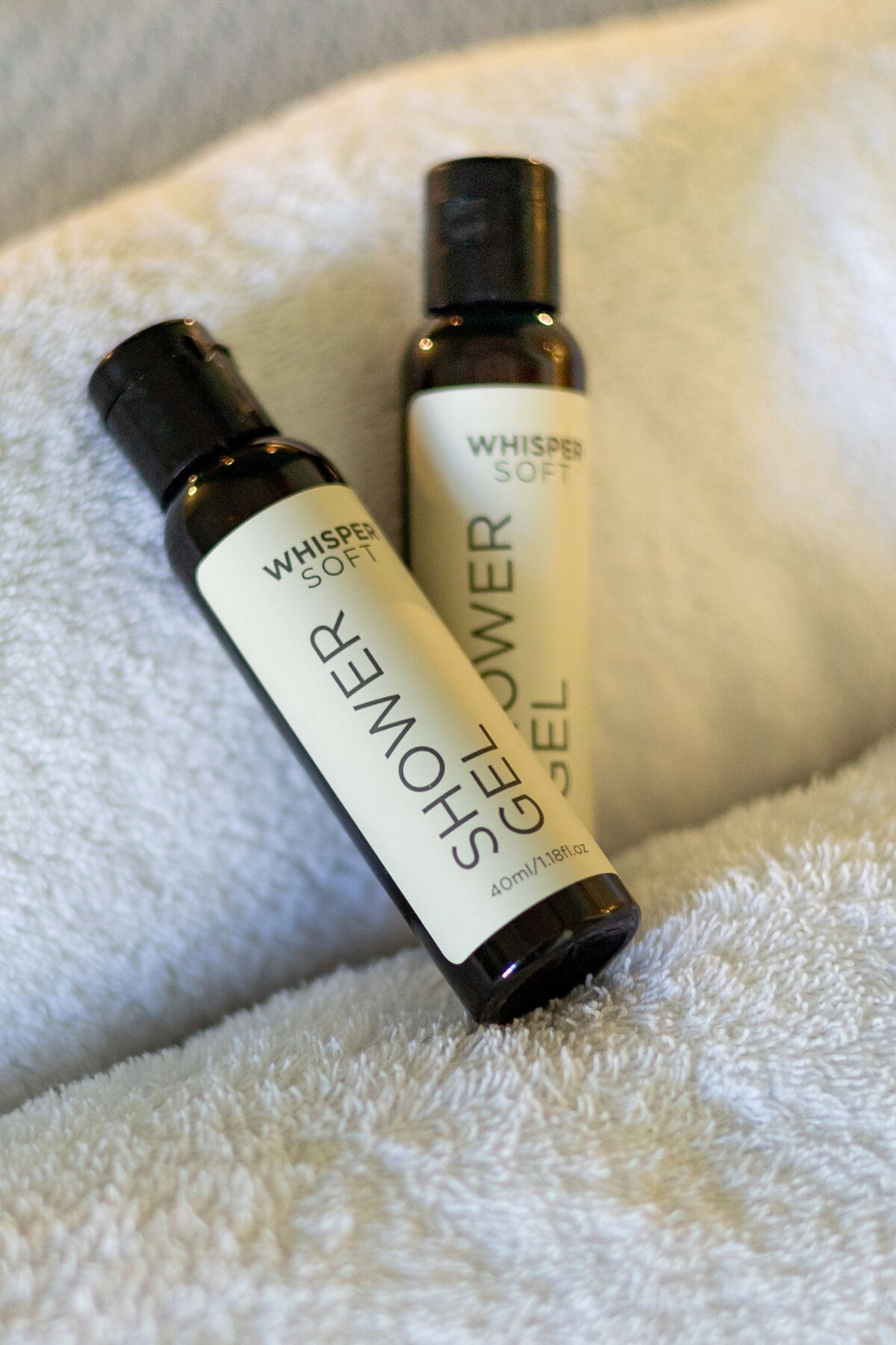 Two bottles of Whisper Soft shower gel on a white towel.