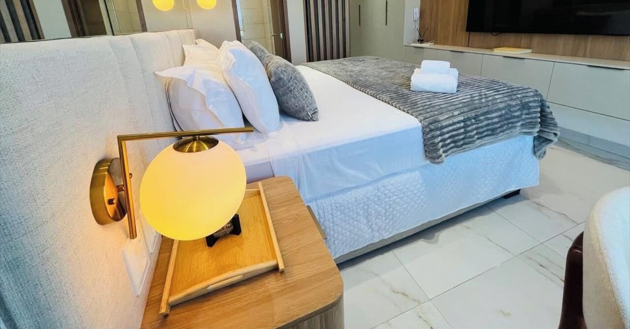 Ein modernes Hotelzimmer mit einem Bett, einem Nachttisch mit Lampe und einem an der Wand montierten Flachbildfernseher.