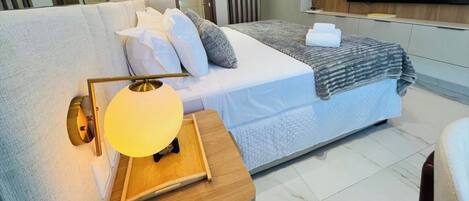 Ein modernes Hotelzimmer mit einem Bett, einem Nachttisch mit Lampe und einem an der Wand montierten Flachbildfernseher.