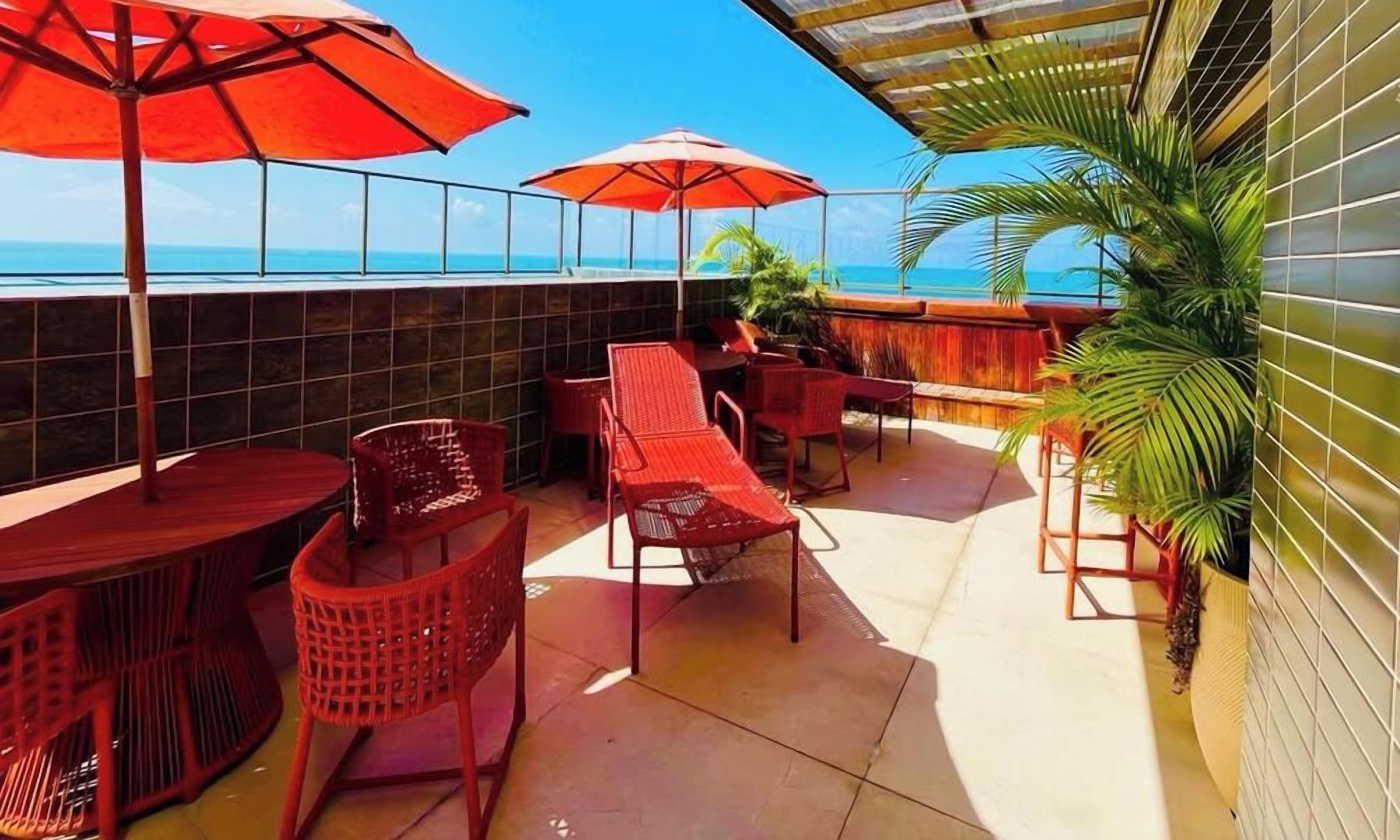 Una terrazza con sedie rosse e ombrelloni, vista sull'oceano e un muro in maiolica.