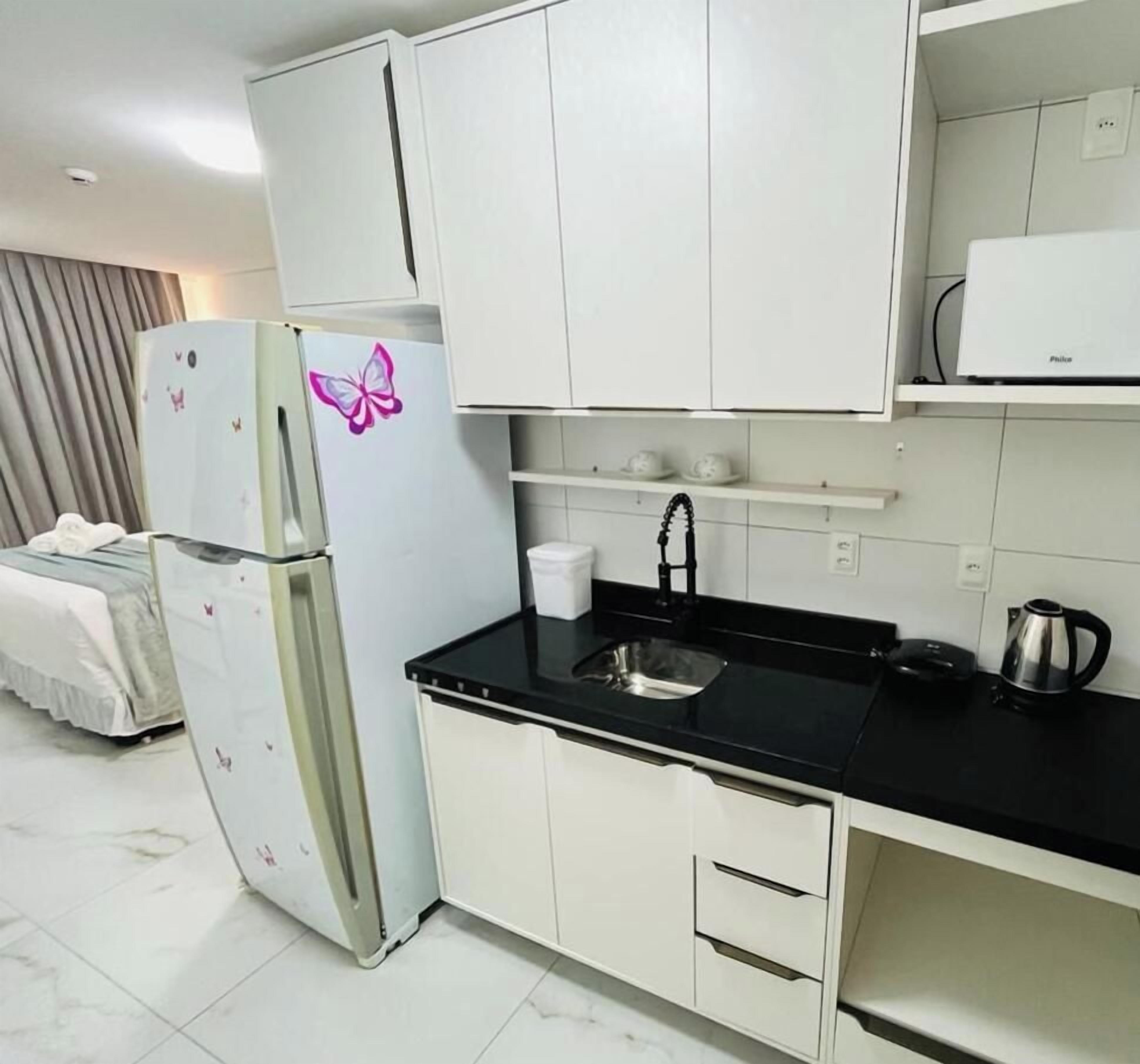 Cocina compacta con armarios blancos, encimera negra, un lavabo y un refrigerador con un adorno de mariposa.