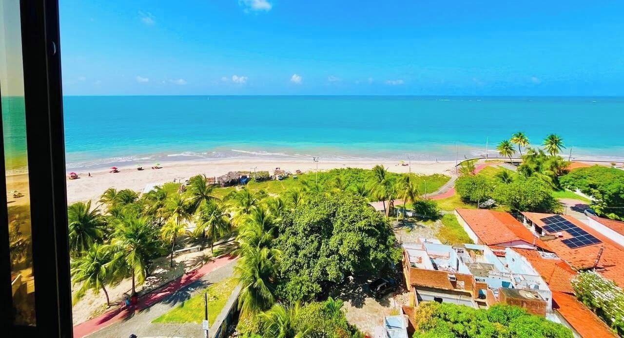 Vista costera con playa, palmeras y edificios con techos rojos.