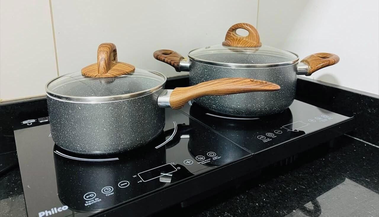 Dos ollas negras con asas de madera sobre una cocina de inducción negra.