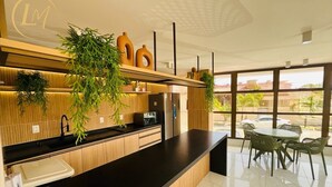 Una cocina moderna con cubierta negra, armarios de madera y un lavamanos integrado. Hay plantas en macetas sobre la cubierta y una zona de comedor con sillas y una mesa.