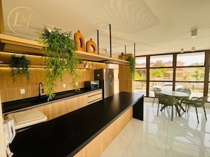 Una cocina moderna con cubierta negra, armarios de madera y un lavamanos integrado. Hay plantas en macetas sobre la cubierta y una zona de comedor con sillas y una mesa.