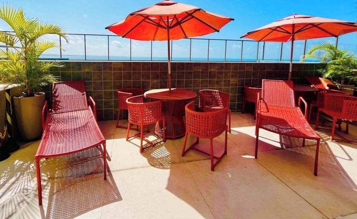 Un patio al aire libre con mobiliario de mimbre rojo y sombrillas, con vista a un cuerpo de agua.