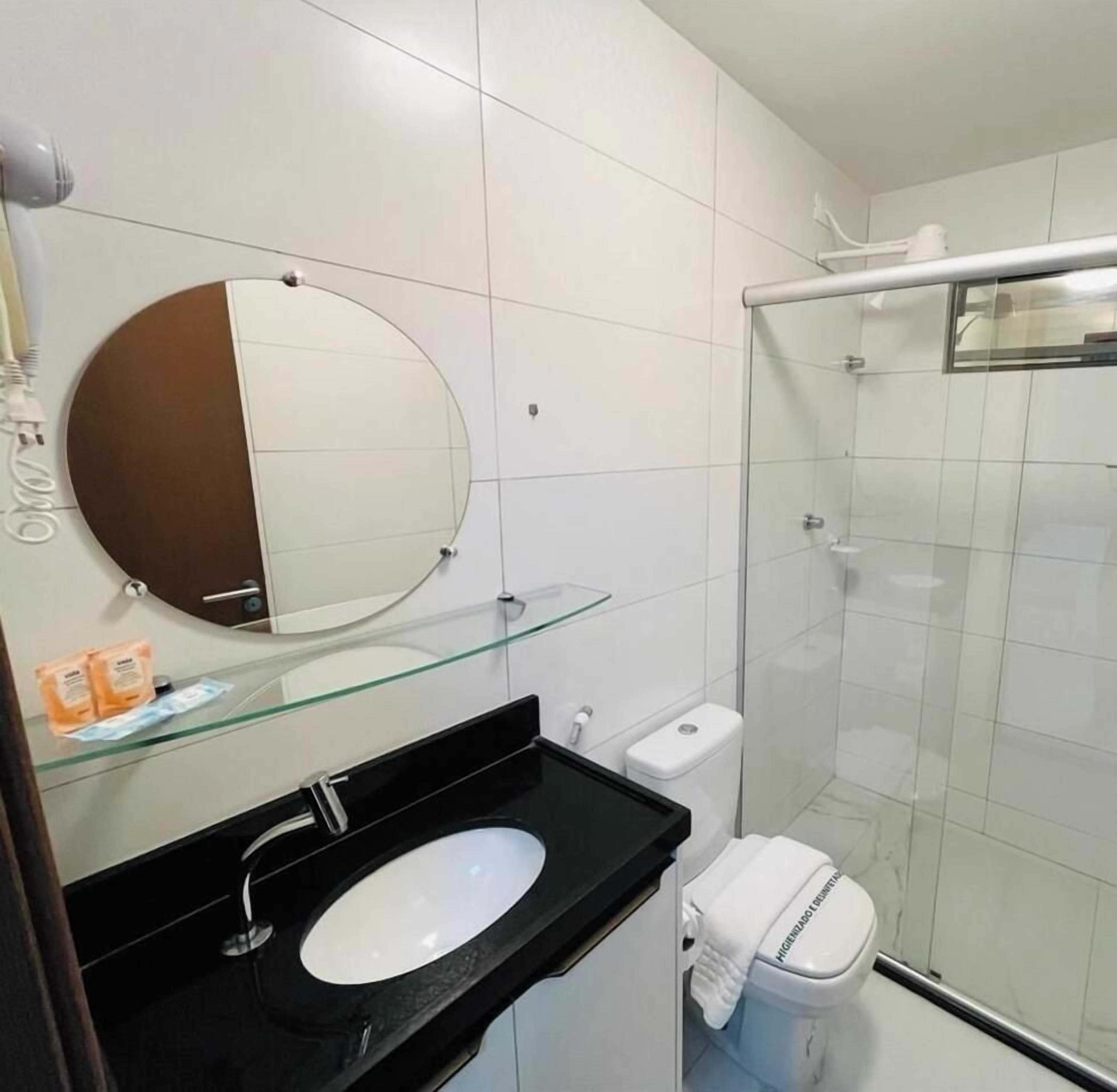 Un baño moderno con cabina de ducha de vidrio, un espejo redondo y un lavabo negro.