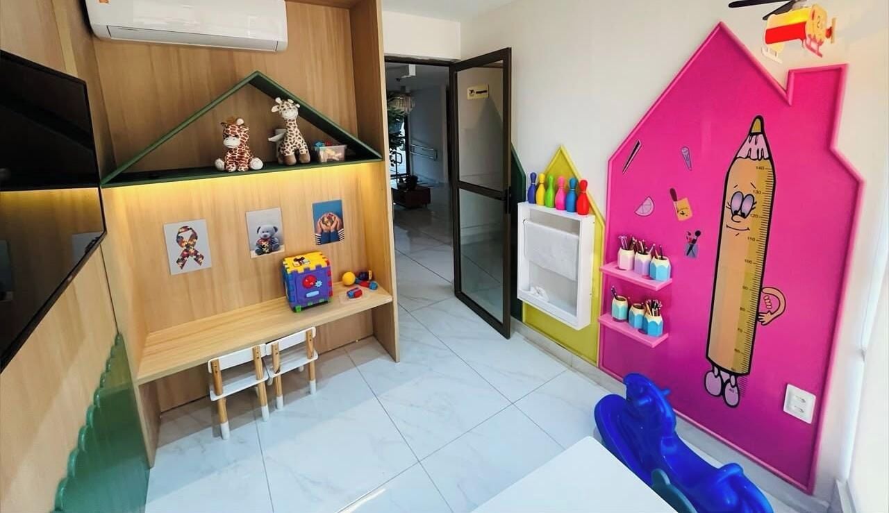 Un cuarto de juegos infantil con un banco de madera, estantes con juguetes y una pared rosa con adornos educativos.