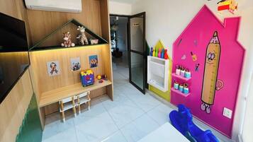 A child's playroom with a wooden bench, shelves with toys, and a pink wall with educational decorations.