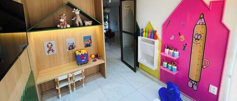 Un cuarto de juegos infantil con un banco de madera, estantes con juguetes y una pared rosa con adornos educativos.
