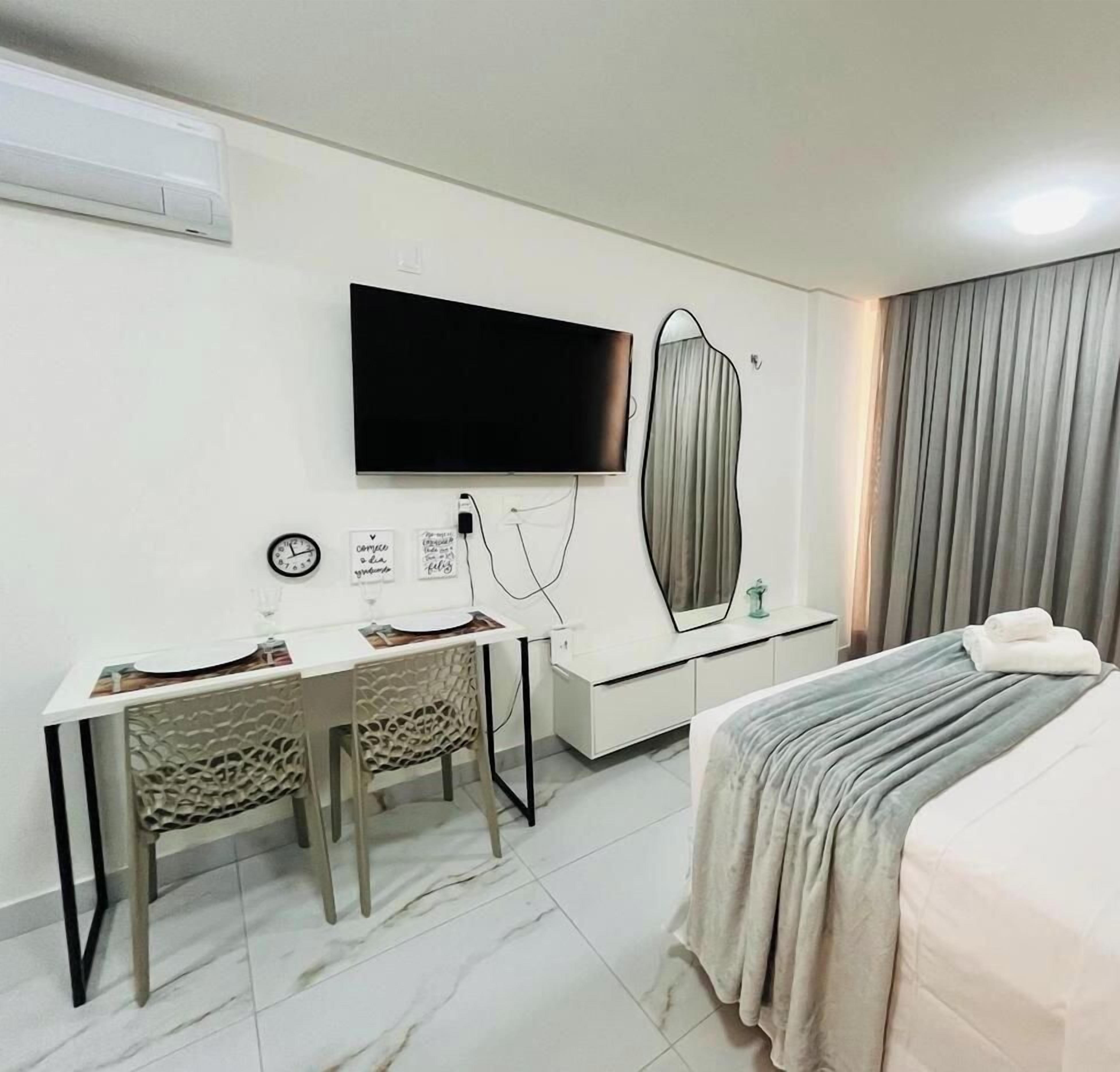 Een hotelkamer met een bed, een bureau met stoel, een flatscreen televisie aan de muur, een klok en een spiegel.