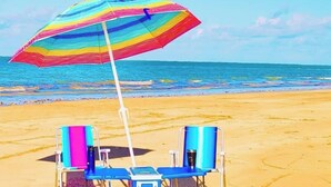 Escena de playa con una sombrilla colorida, dos sillas de playa y una nevera.