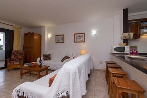 Ein Wohnzimmer mit einer Couch, einem Holztisch, einem Schrank und einer Küchenzeile mit Mikrowelle und Toaster.