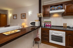 A compact kitchen with a microwave, oven, and a small stool. - Paloma Beach 16 - One Bed (Los Cristianos)