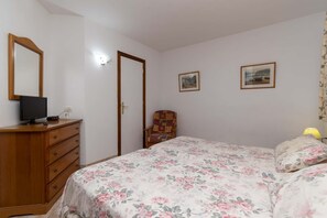 Ein Schlafzimmer mit einem Bett, einem Schminktisch, einem Sessel und zwei gerahmten Bildern an der Wand.