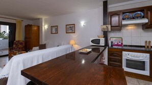 Ein Zimmer mit Esstisch aus Holz, einer Couch, einem Bett, einer Mikrowelle, einem Backofen und einer Vitrine mit dekorativen Tellern.