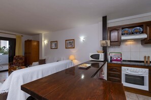 Ein Zimmer mit Esstisch aus Holz, einer Couch, einem Bett, einer Mikrowelle, einem Backofen und einer Vitrine mit dekorativen Tellern.