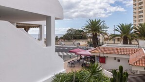 Ein Balkon mit Blick auf eine Straße, Palmen und ein Gebäude mit Ziegeldach.