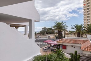 Ein Balkon mit Blick auf eine Straße, Palmen und ein Gebäude mit Ziegeldach.
