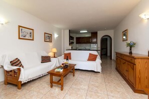 Ein Wohnzimmer mit Sofa, Couchtisch und Schrank. Im Hintergrund ist eine Küche zu sehen.
