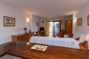 A hotel room with a bed, a wooden desk, a television, and a dining area with a table and chairs. - Paloma Beach 16 - One Bed (Los Cristianos)