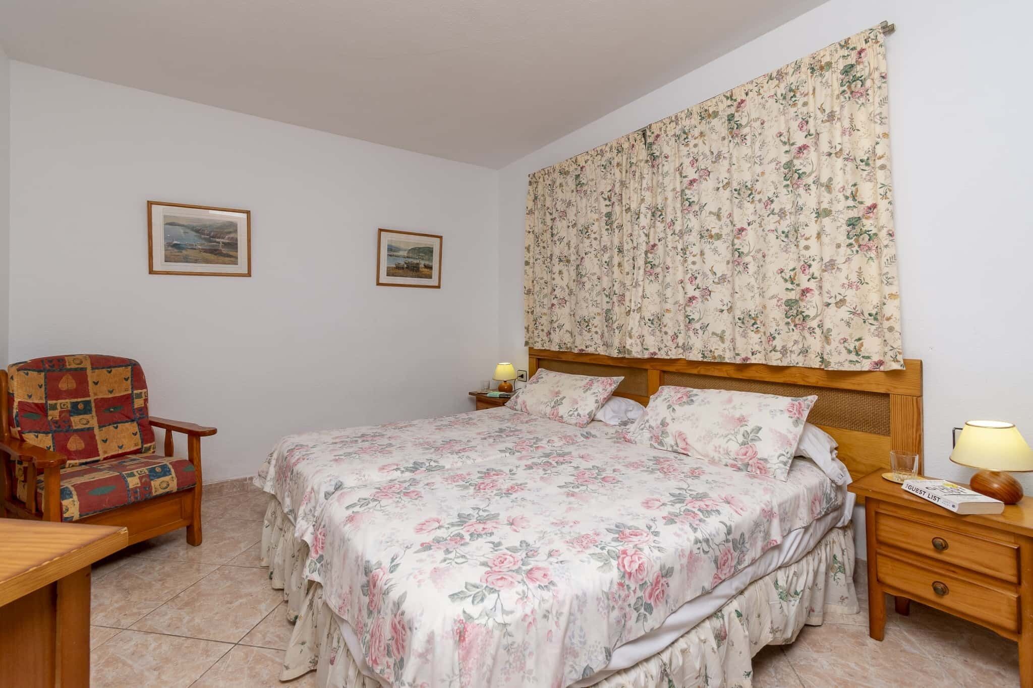 A bedroom with a bed, a chair, a nightstand, and two framed pictures on the wall.