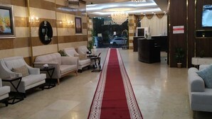 Un vestíbulo de hotel con alfombra roja, zona de estar, candelabro y mostrador de recepción.