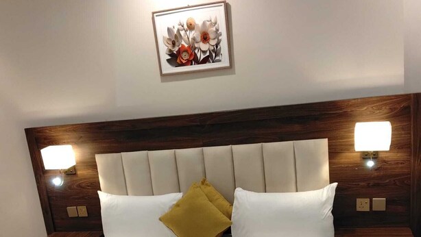 Habitación de hotel con una cama grande, dos mesitas de noche, cabecera con iluminación integrada y una obra de arte enmarcada sobre la cama.
