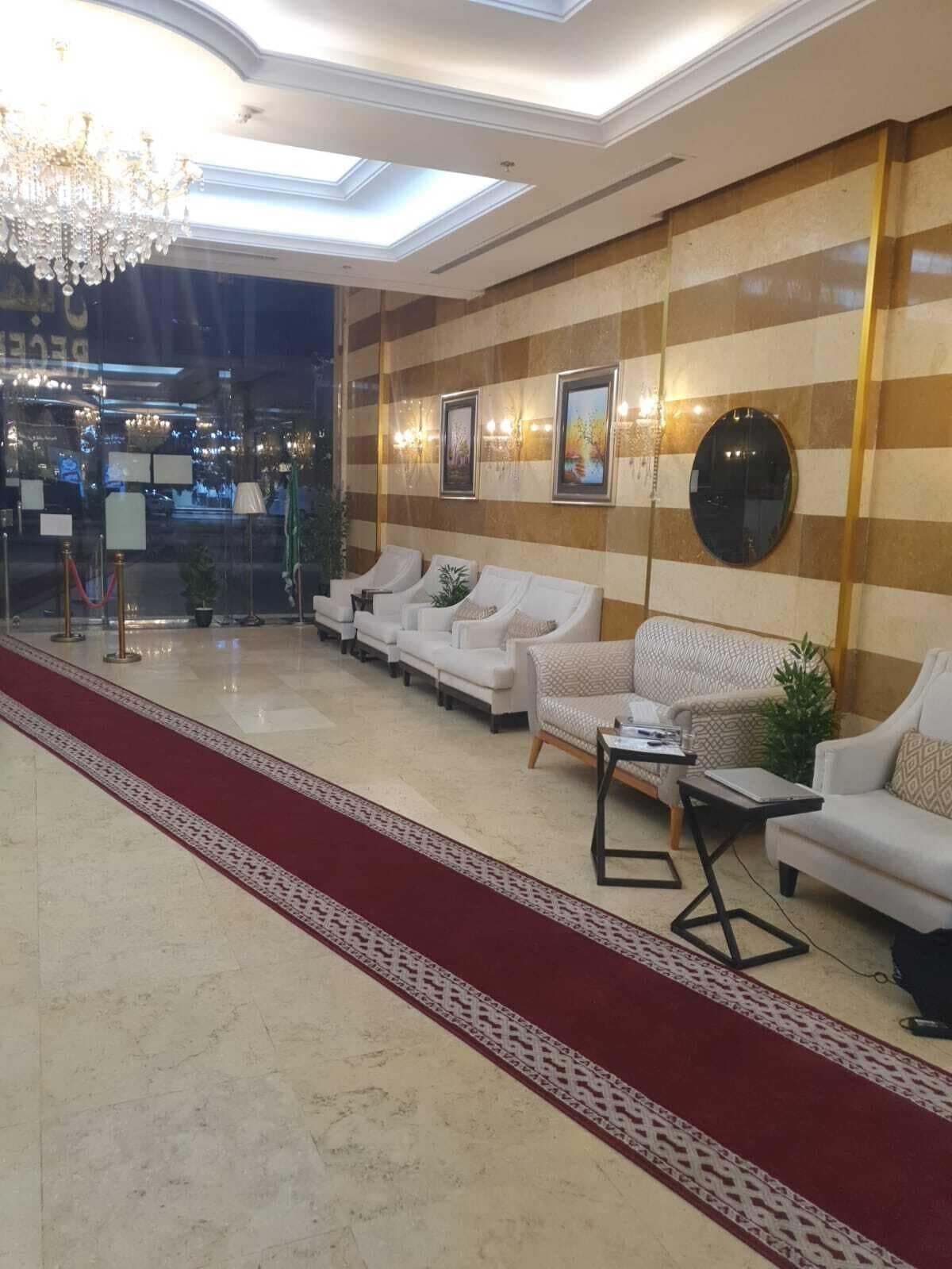 Un hall d’hôtel avec un tapis rouge, des canapés blancs, un lustre et des œuvres d’art encadrées accrochées aux murs.