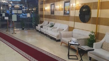 Un hall d’hôtel avec un tapis rouge, des canapés blancs, un lustre et des œuvres d’art encadrées accrochées aux murs.