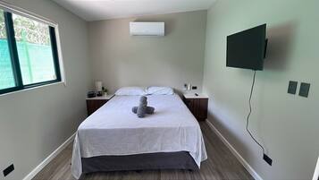 A bedroom with a bed, bedside tables, a TV mounted on the wall, and an air conditioning unit.